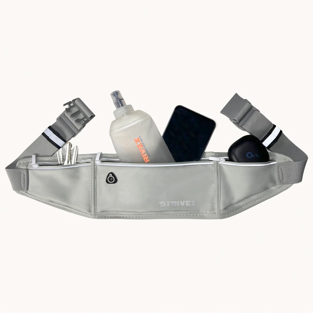 A light gray Strive brand waist bag filled with various items like a water bottle, phone, and earbud case, shown against a plain off-white background.