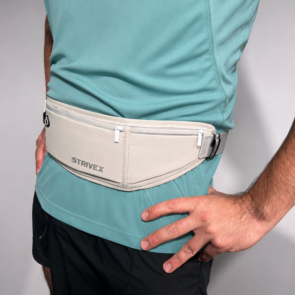 A close-up of a person wearing a light grey Strivex waist pack pouch over a teal athletic shirt and black shorts, with both hands resting on the hips.