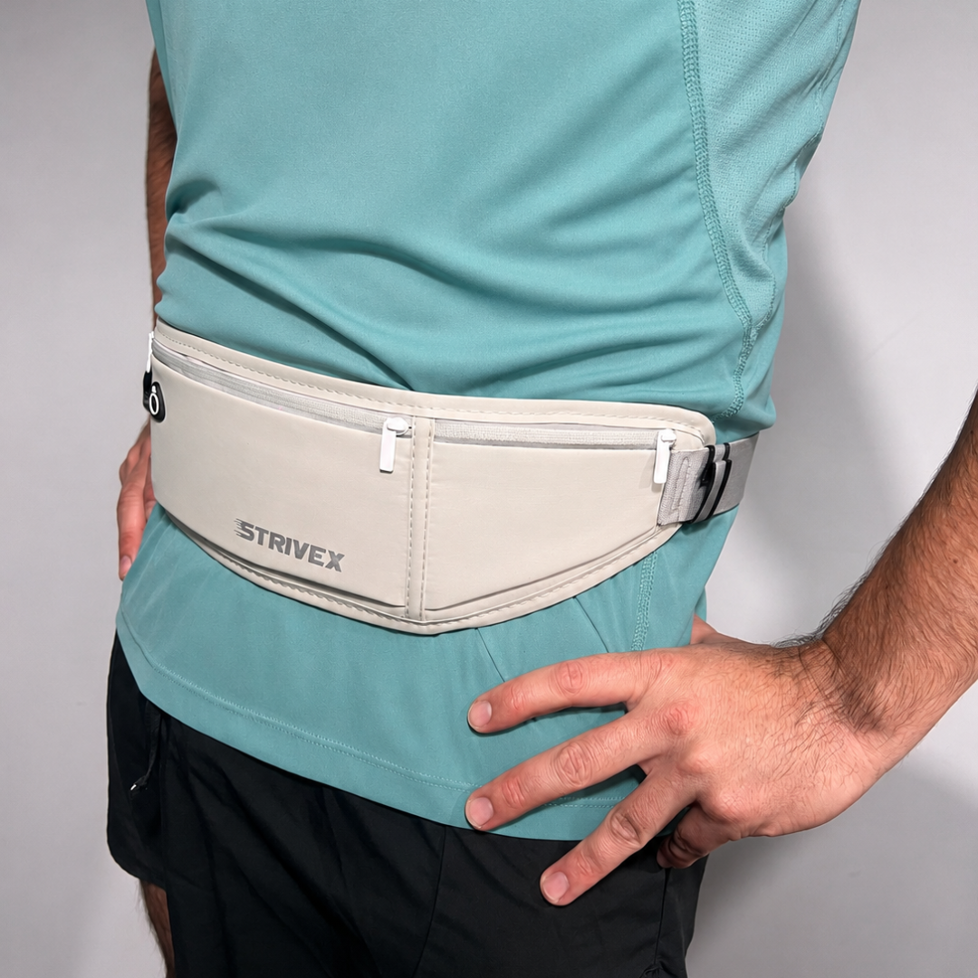 A close-up of a person wearing a light grey Strivex waist pack pouch over a teal athletic shirt and black shorts, with both hands resting on the hips.
