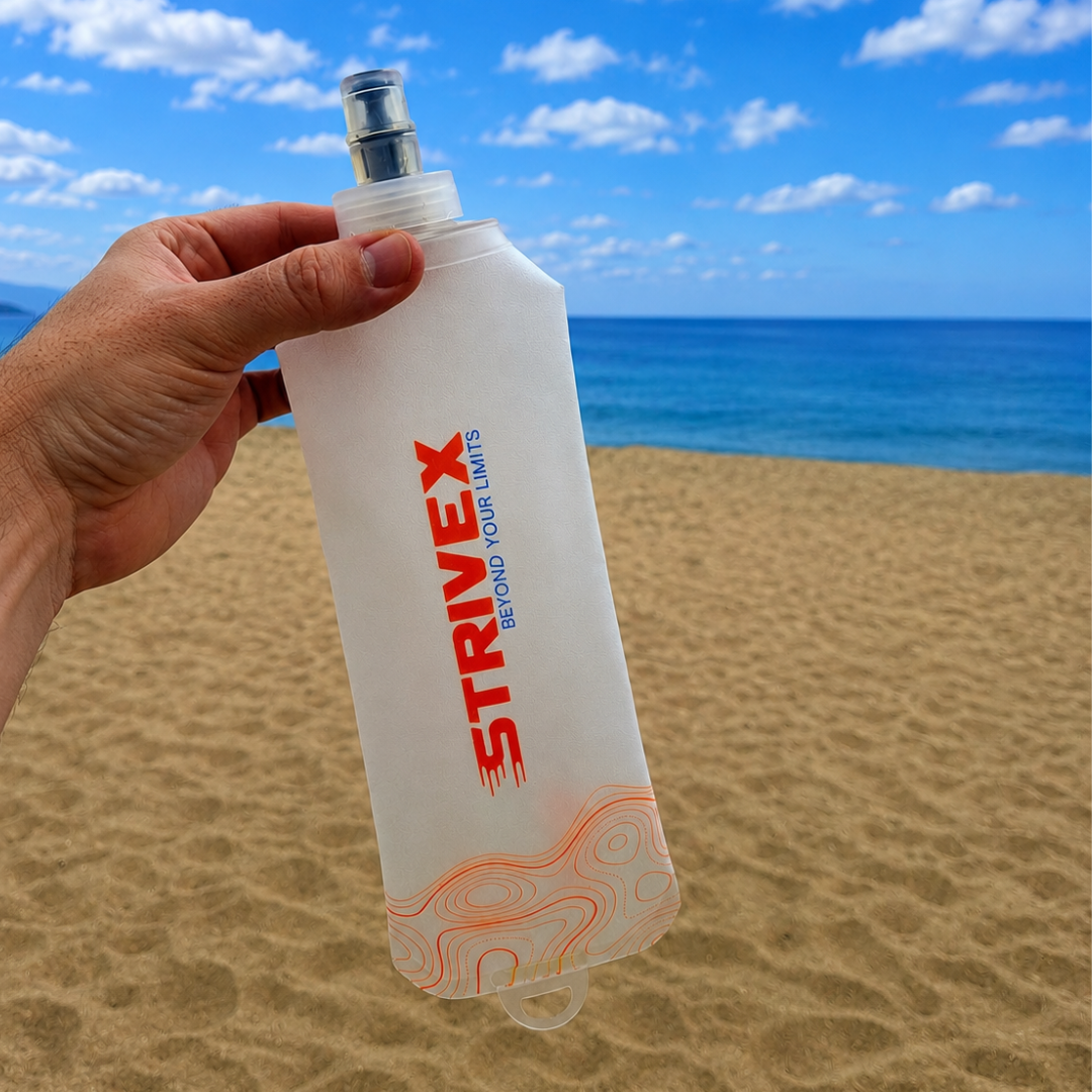 Hand holding a Strivex bottle soft flask wave hook 500 on a beach with ocean and sky in the background